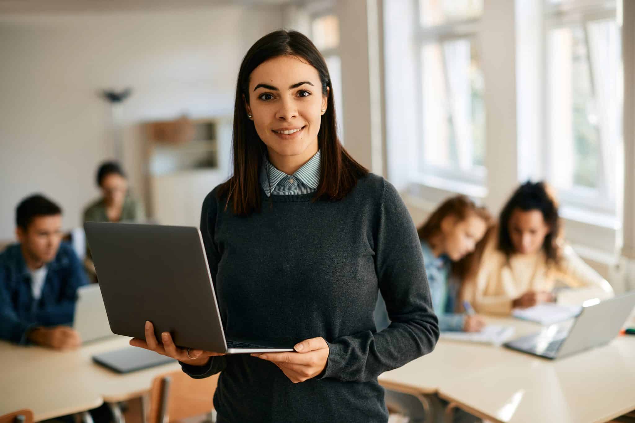 smiling computer science teacher using laptop during class