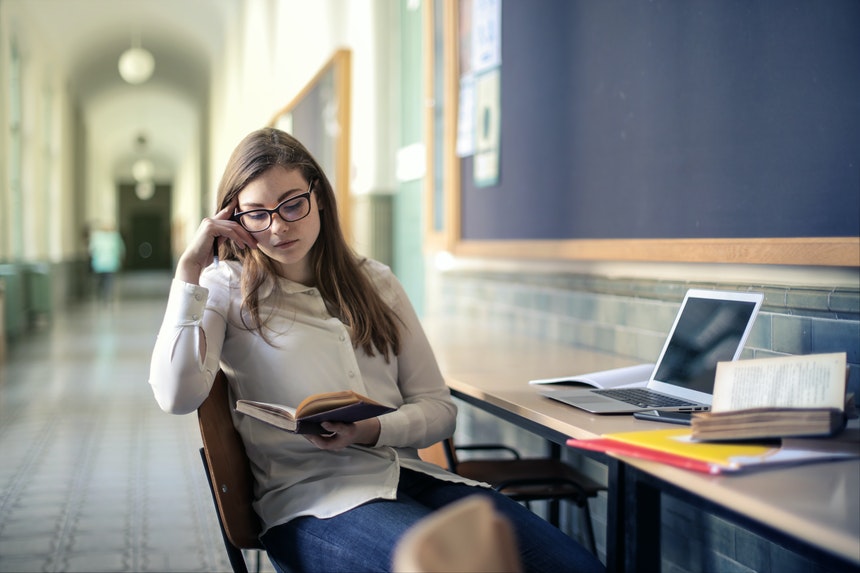 Woman studying for entrance exam with books and laptop on the table