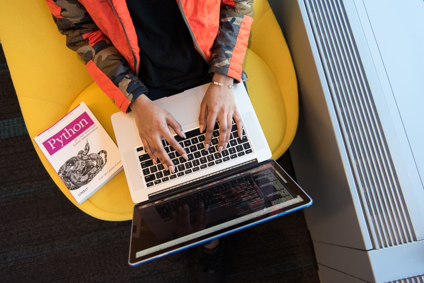 Woman with a Python programming book coding in her Macbook